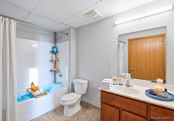 A bathroom with a white toilet, a bathtub with a blue tint, and a wooden vanity with a mirror.