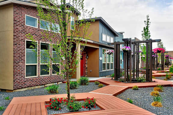 A modern house with a red door and a wooden walkway leading to the entrance at Verraso Village Townhomes in Meridian, 83646