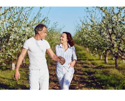 A man and a woman are walking hand in hand in an apple orchard.