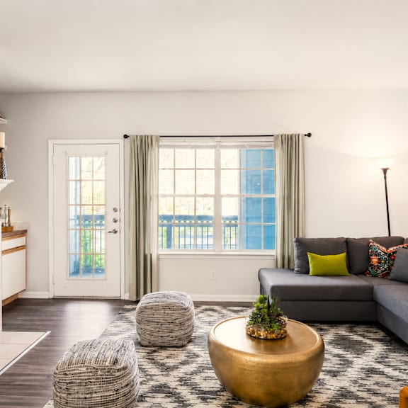 A modern living room with a grey sofa, a wooden coffee table, and a kitchen area in the background.
