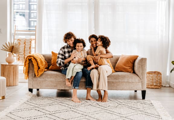 A family of four is sitting on a couch in a bright room.