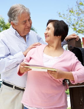 An older man and woman are standing outside, with the man holding a book and the woman holding a plate.