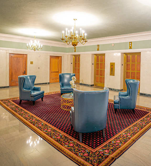 A room with a chandelier, four chairs, and a rug.