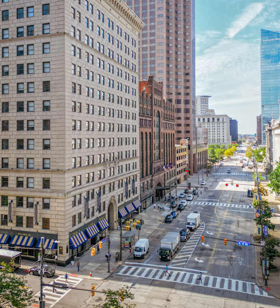A city street with cars and trucks driving and pedestrians crossing the street.