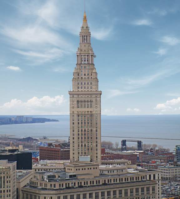 A tall building with a spire on top stands in the foreground of a cityscape.