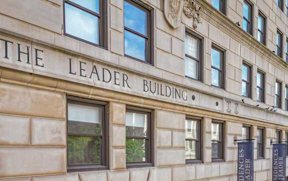 The Leader Building is a large, beige, stone building with a large arched entrance.