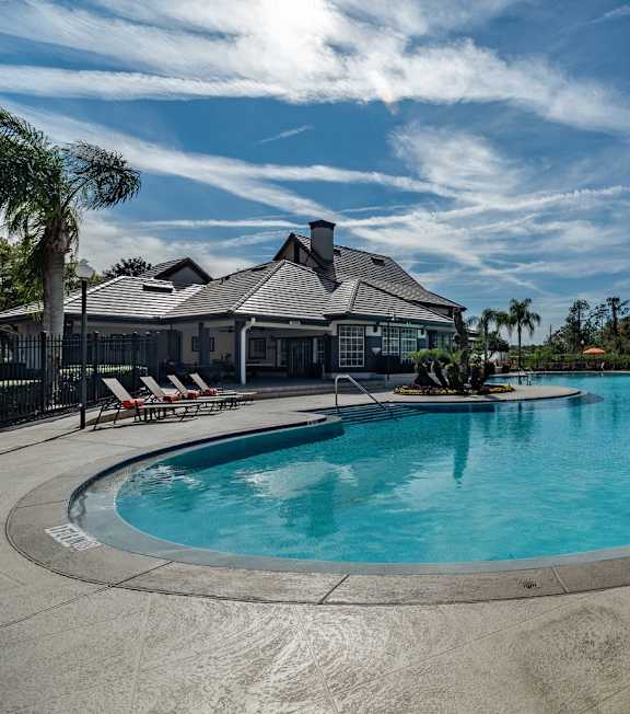 A swimming pool surrounded by a tiled patio and lounge chairs in front of a building with palm trees. at Park Place Oviedo Apartments, Oviedo, FL