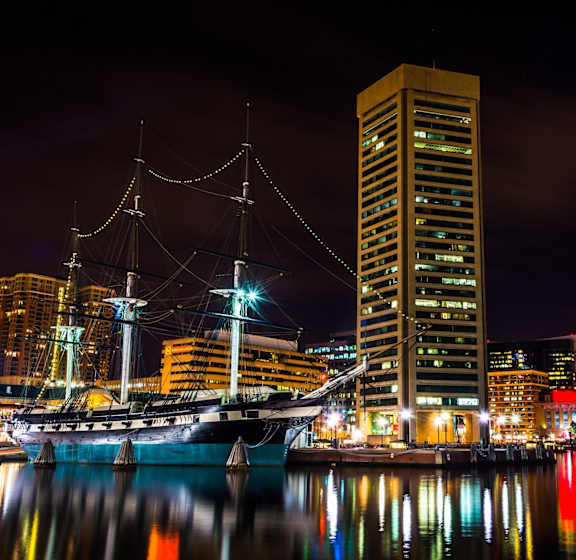 A tall ship is docked in a harbor at night.