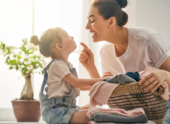 A woman and a child are sitting together, with the woman holding a basket of clothes.