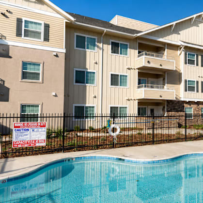 A swimming pool in front of a residential building with a sign that says "Caution: Capacity Limit".