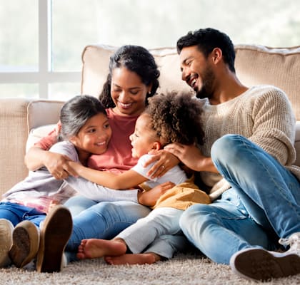 A family of four is sitting on the floor in a living room.
