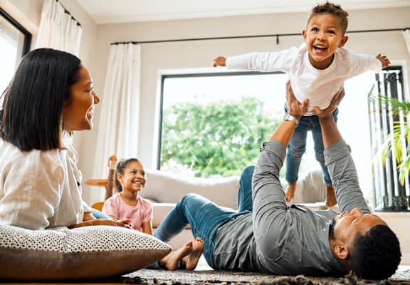 A man is lifting a child in the air while two others watch.