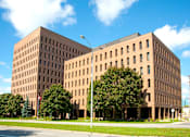 Thumbnail 1 of 4 - A large brown building with a flag on the left side.