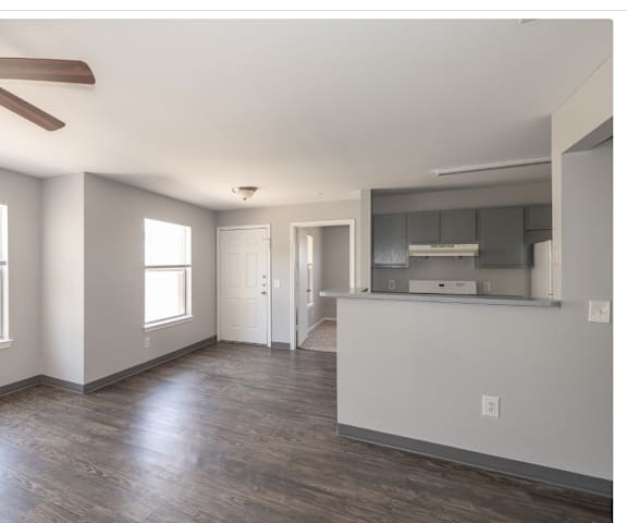 an empty living room with a ceiling fan and a kitchen