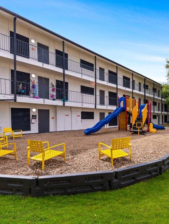 a courtyard with a playground and yellow chairs in front of an apartment building