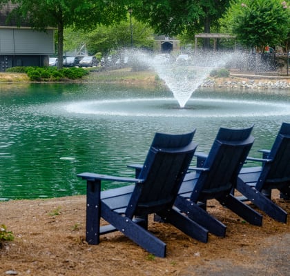 a row of blue adirondack chairs sit in front of a fountain in a pond