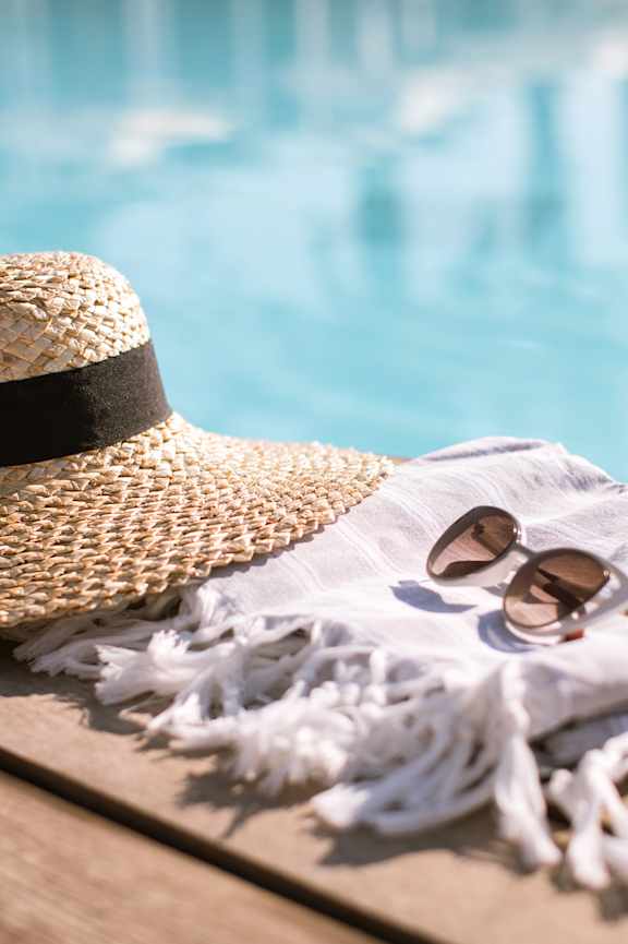 A straw hat and sunglasses and a white scarf are placed on a wooden surface