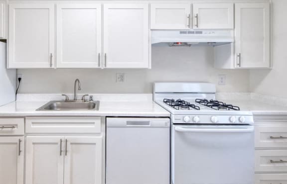 A white kitchen with a refrigerator, stove, and sink.