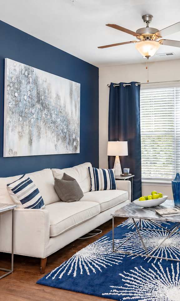 A living room with a white couch, a blue rug, and a ceiling fan.