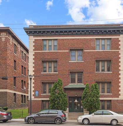 A row of red brick buildings with cars parked in front.