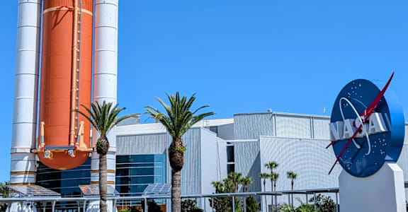 A large orange and white rocket with two boosters stands in front of a building with a large NASA logo. at The Teale New Haven Apartments, Melbourne, FL, 32904
