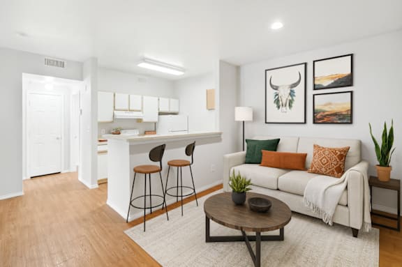 A living room with a white couch, a coffee table, and a kitchen area in the background.
