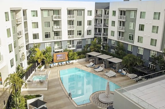 A swimming pool surrounded by lounge chairs and umbrellas in front of apartment buildings.
