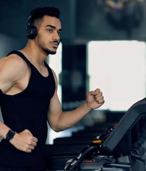 A man in a black tank top is running on a treadmill.