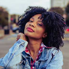 A woman with curly hair wearing a denim jacket is posing for a picture.