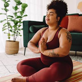 A woman in a red outfit is meditating on a yoga mat.