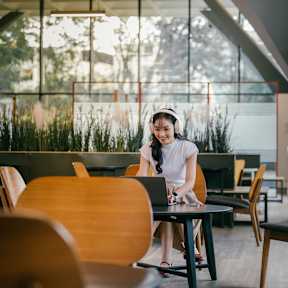 A woman is sitting at a table in a modern cafe with wooden chairs and tables.