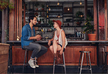 Two people sitting at a bar, one wearing a blue shirt and the other a red hat.