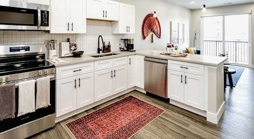 A kitchen with white cabinets and a red rug on the floor.
