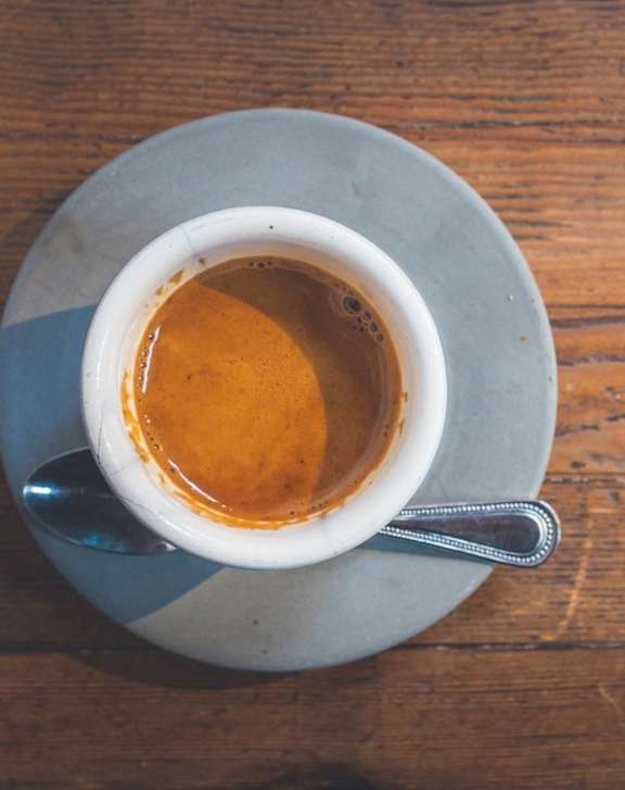 A cup of coffee on a saucer with a spoon.