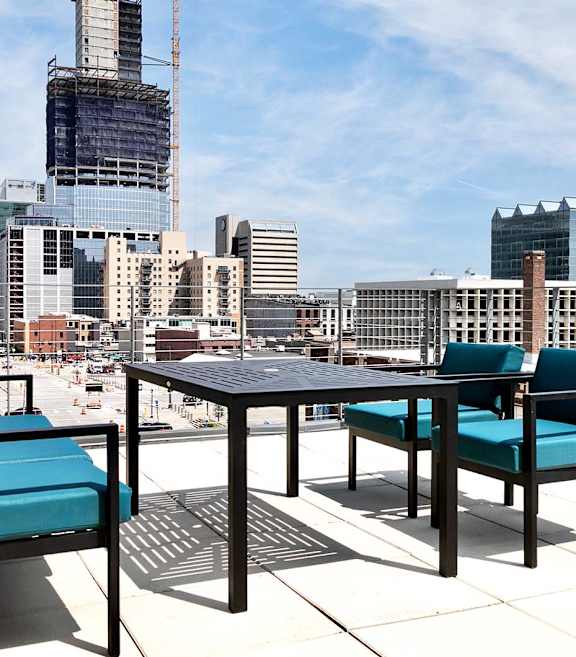 A table and two chairs are on a patio with a city skyline in the background.
