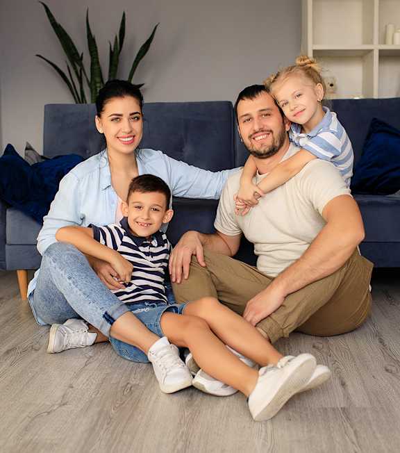 A family of three sits together on the floor in a living room.