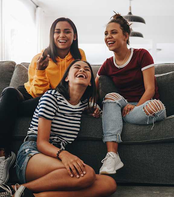 Three women are sitting on a couch, laughing and enjoying each other's company.