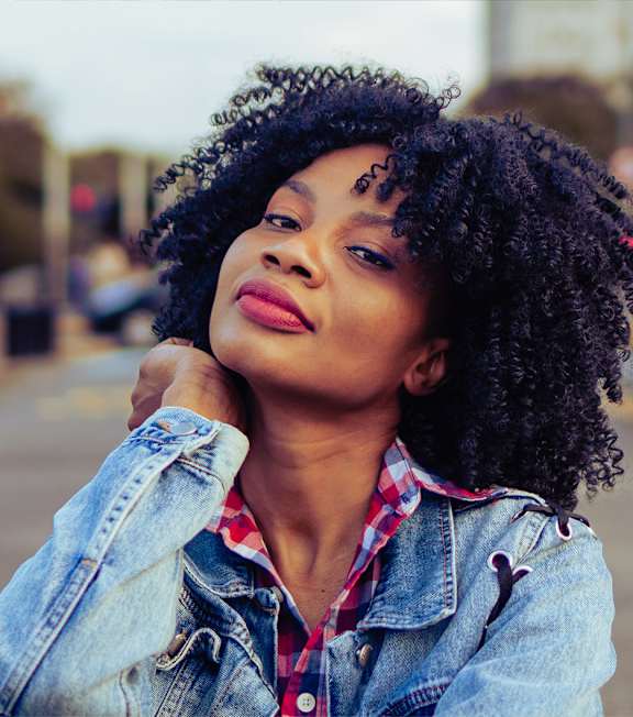 A woman with curly hair wearing a denim jacket is posing for a picture.