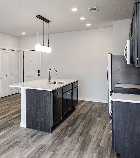 A kitchen with a white counter top and dark wood flooring.