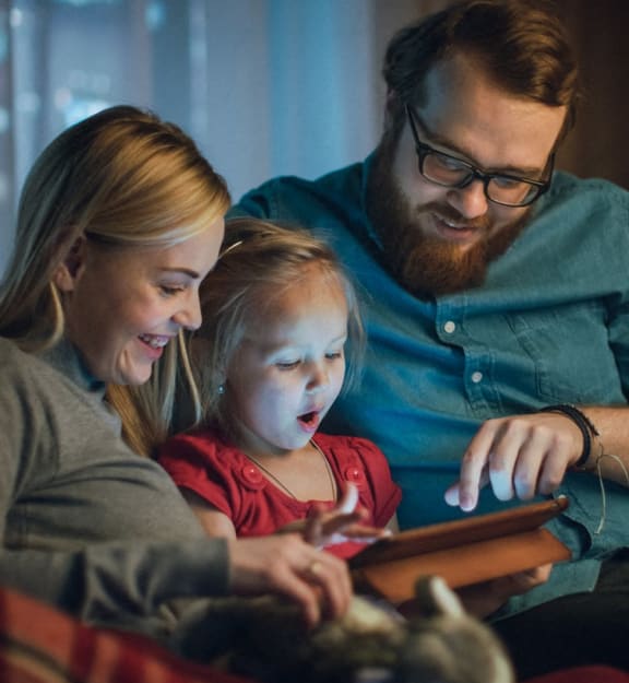 a family sitting on a couch looking at a tablet computer