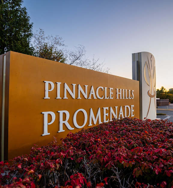 A sign for Pinnacle Hills Promenade is surrounded by red foliage.