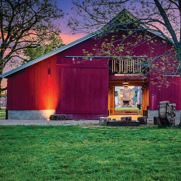 a red and purple barn with a tree in front of it