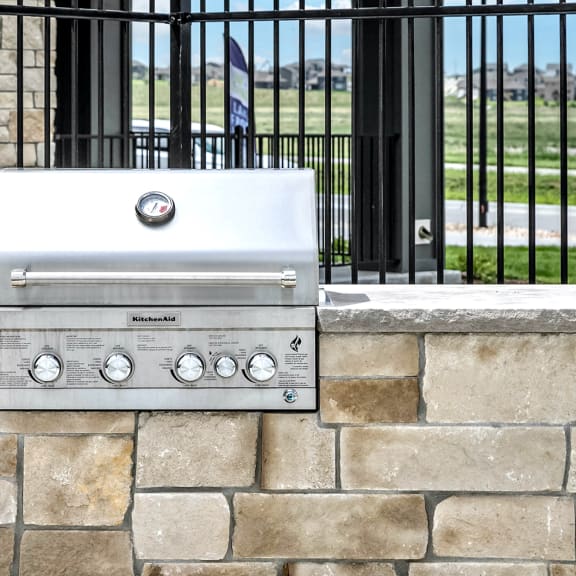 an outdoor grill on a stone wall with a wrought iron fence in the background