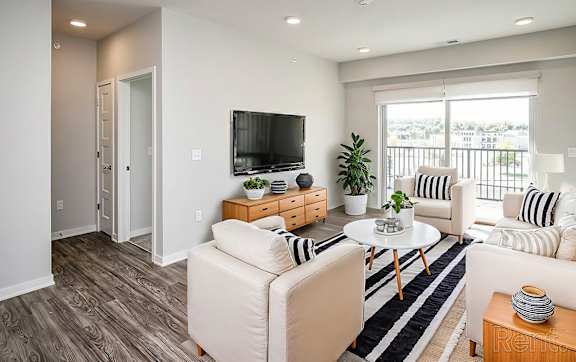 A living room with a white couch, a wooden coffee table, and a flat-screen TV mounted on the wall.