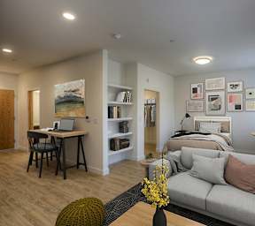 A living room with a grey couch and a desk with a laptop.