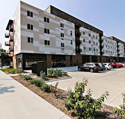 A modern building with a white and beige facade and a parking lot in front.