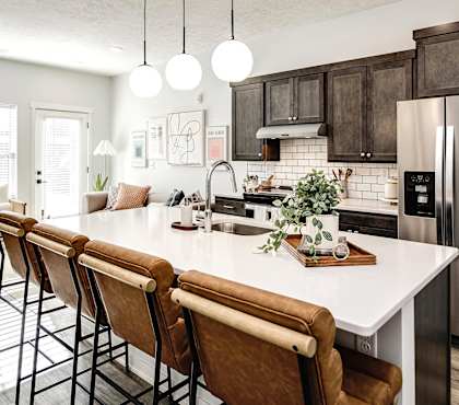 A modern kitchen with a white island and brown barstools.