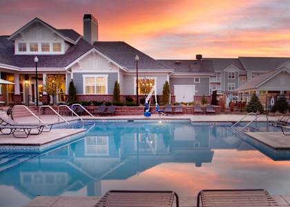 A swimming pool in front of a house with a sunset in the background.