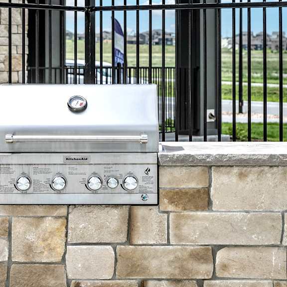 an outdoor grill on a stone wall with a wrought iron fence in the background
