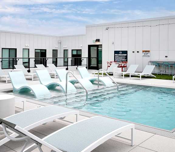 A pool with sun loungers and a white building in the background.